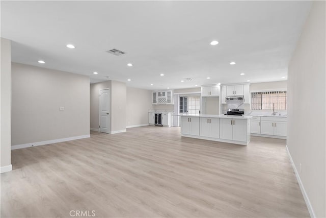 unfurnished living room featuring baseboards, light wood-style flooring, recessed lighting, wine cooler, and a sink