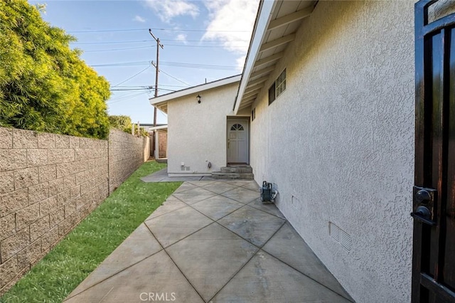 view of exterior entry with stucco siding, fence, and a patio area