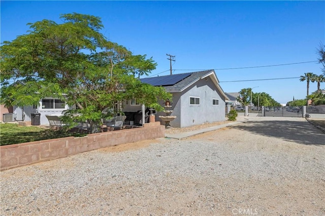 5136 W W Ave L8, Lancaster, CA 93536 - view of front facade with roof mounted solar panels, gravel driveway, stucco siding, a gate, and central AC