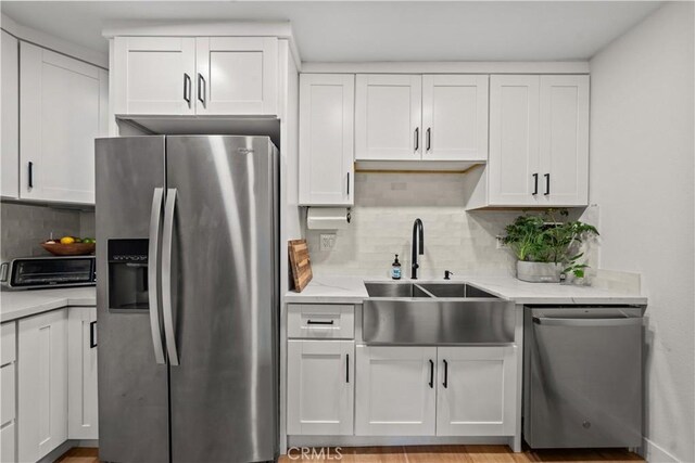 kitchen with stainless steel appliances, a sink, white cabinetry, decorative backsplash, and light stone counters