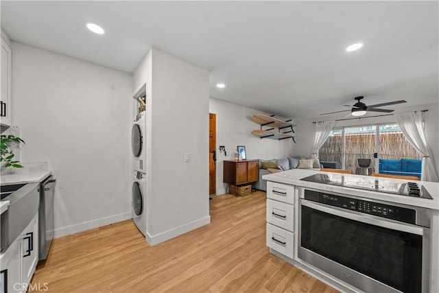 kitchen with appliances with stainless steel finishes, stacked washer and clothes dryer, white cabinets, a ceiling fan, and light wood finished floors