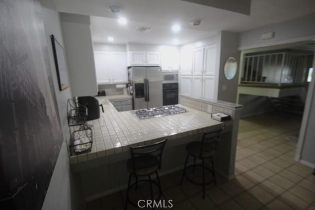 19555 Chadway St, Canyon Country, CA 91351 - kitchen with appliances with stainless steel finishes, tile counters, a peninsula, white cabinetry, and a kitchen bar