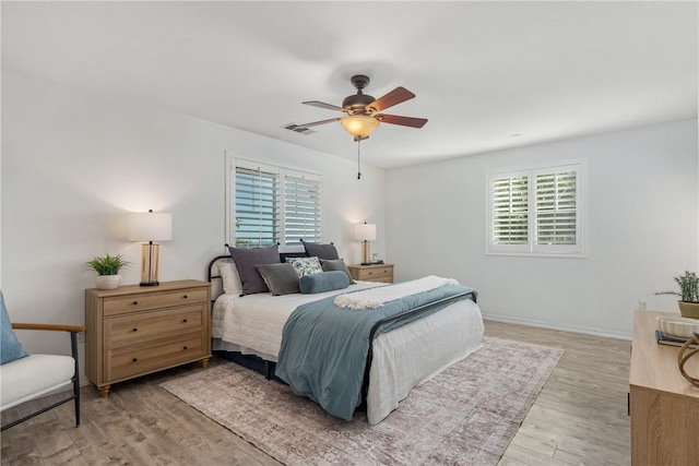 bedroom with multiple windows, light wood-style flooring, baseboards, and ceiling fan