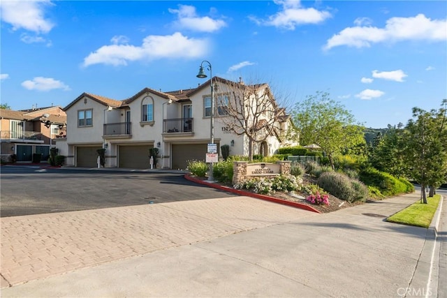 view of front of property featuring driveway, an attached garage, stucco siding, a residential view, and a balcony