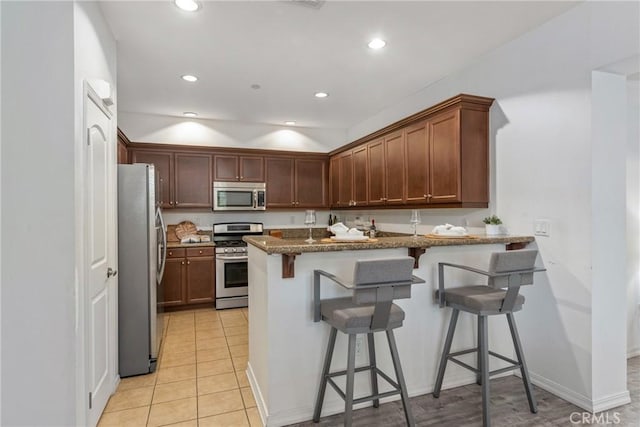kitchen with stainless steel appliances, a peninsula, a breakfast bar area, recessed lighting, and dark stone counters