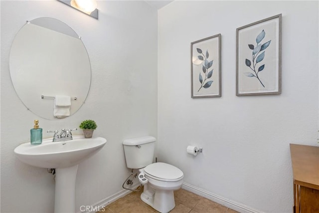 half bath with toilet, baseboards, and tile patterned floors