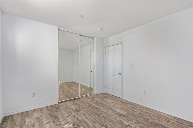 unfurnished bedroom with wood finished floors, baseboards, and a closet