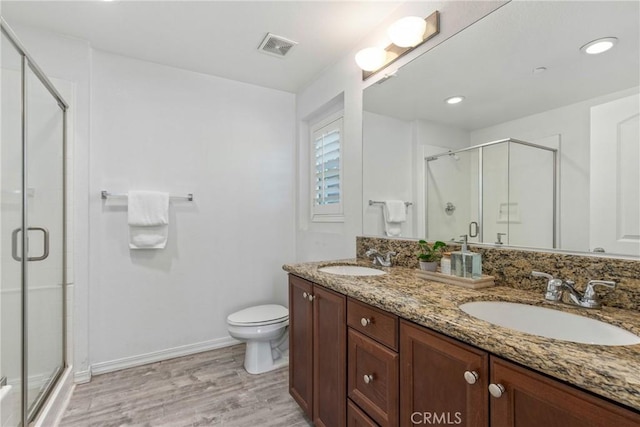 full bath with wood finished floors, a shower stall, double vanity, and toilet