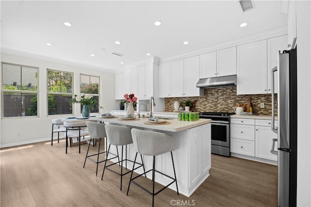 kitchen with stainless steel appliances, under cabinet range hood, ornamental molding, white cabinets, and backsplash