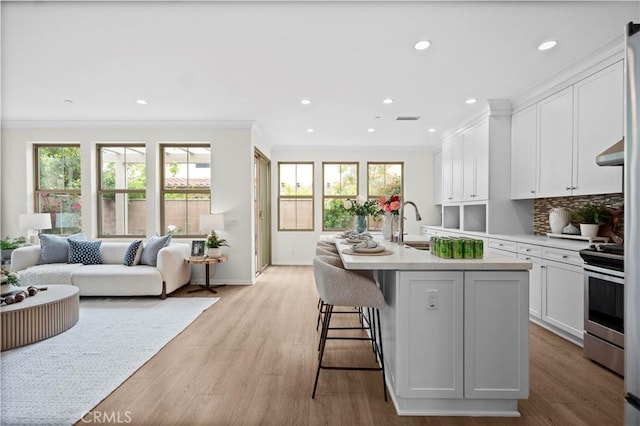 kitchen featuring ornamental molding, stainless steel range with gas stovetop, light countertops, white cabinets, and wall chimney range hood