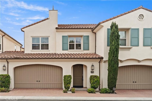 mediterranean / spanish-style home featuring an attached garage, a tile roof, and stucco siding