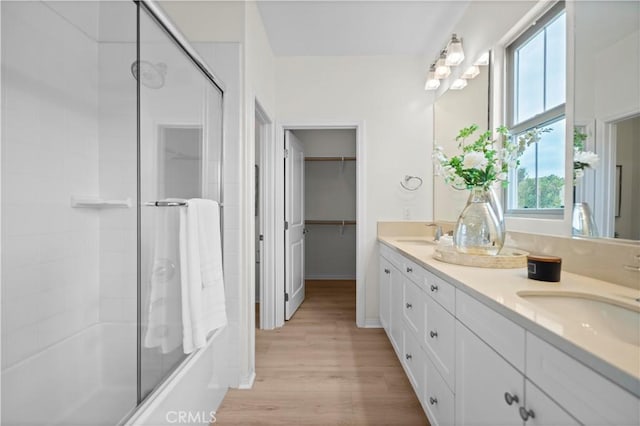 bathroom featuring wood finished floors, double vanity, shower / bath combination with glass door, and a spacious closet