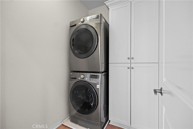 washroom with estacked washer and dryer, cabinet space, baseboards, and wood finished floors