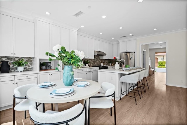 kitchen featuring under cabinet range hood, a kitchen island with sink, white cabinetry, freestanding refrigerator, and tasteful backsplash