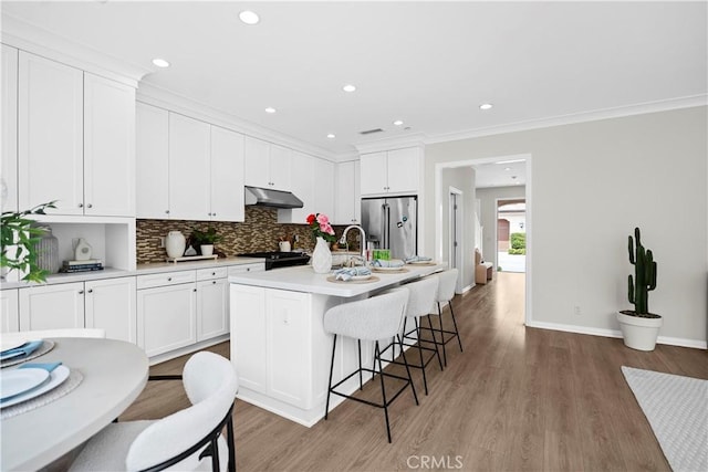 kitchen featuring under cabinet range hood, stainless steel fridge, range, decorative backsplash, and light wood finished floors