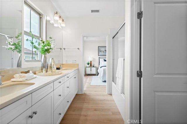 bathroom featuring wood finished floors, double vanity, a shower with shower door, and ensuite bathroom