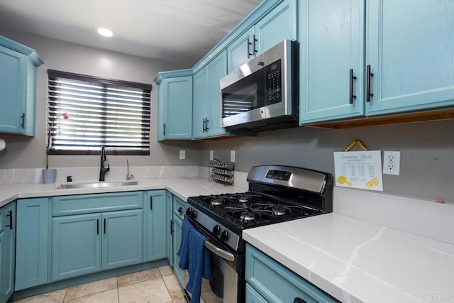 kitchen featuring stainless steel appliances, a sink, blue cabinets, light countertops, and light tile patterned flooring