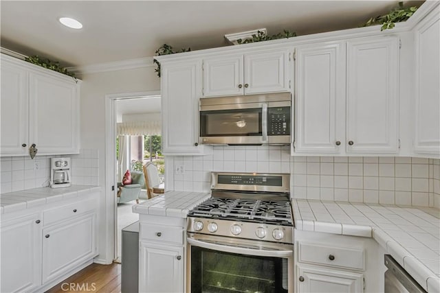 19628 Pine Valley Ave, Porter Ranch, CA 91326 - kitchen with stainless steel appliances, tile countertops, white cabinetry, decorative backsplash, and crown molding