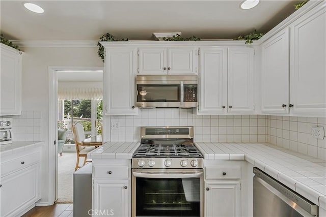 19628 Pine Valley Ave, Porter Ranch, CA 91326 - kitchen featuring appliances with stainless steel finishes, tile countertops, white cabinets, and crown molding