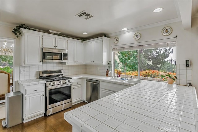 19628 Pine Valley Ave, Porter Ranch, CA 91326 - kitchen featuring appliances with stainless steel finishes, tile counters, a sink, white cabinets, and ornamental molding