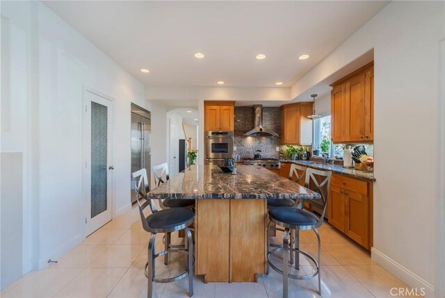 428 12th St, Huntington Beach, CA 92648 - kitchen featuring wall chimney exhaust hood, brown cabinetry, a breakfast bar area, backsplash, and a kitchen island