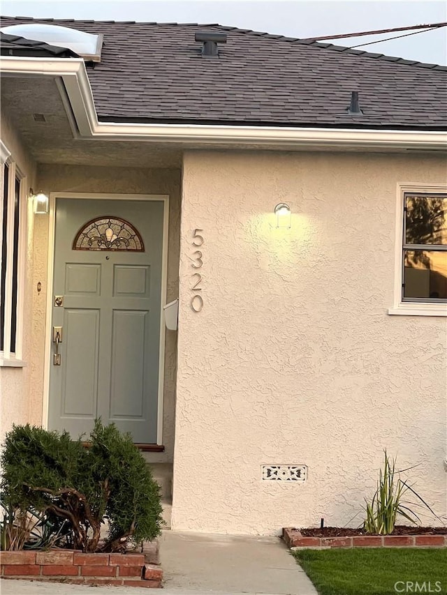 doorway to property with a shingled roof and stucco siding