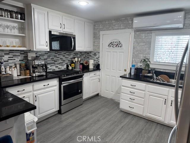 807 N Pearl Ave, Compton, CA 90221 - kitchen featuring stainless steel appliances, an AC wall unit, white cabinets, and dark countertops