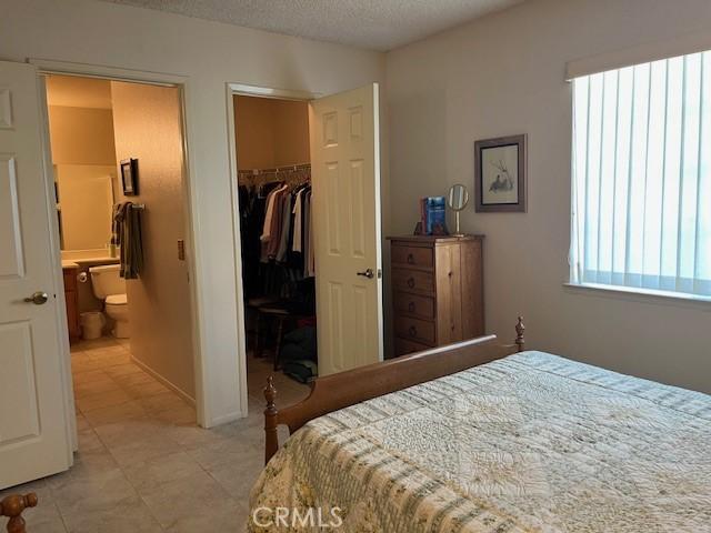 3060 Summer Set Cir, Banning, CA 92220 - bedroom featuring a spacious closet, a closet, ensuite bath, a textured ceiling, and light tile patterned floors