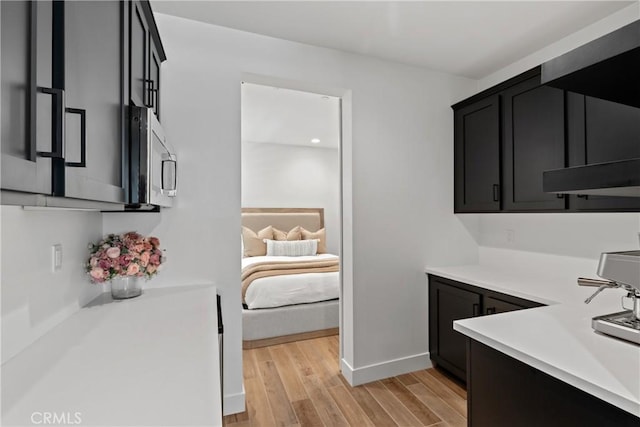 kitchen with stainless steel microwave, light countertops, light wood-type flooring, baseboards, and dark cabinetry