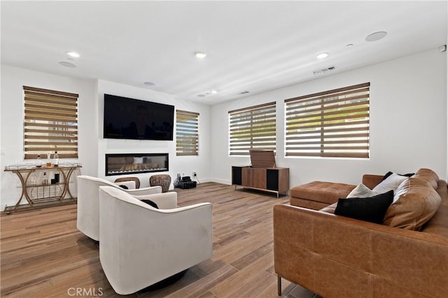 living area with light wood-type flooring, recessed lighting, a glass covered fireplace, and baseboards