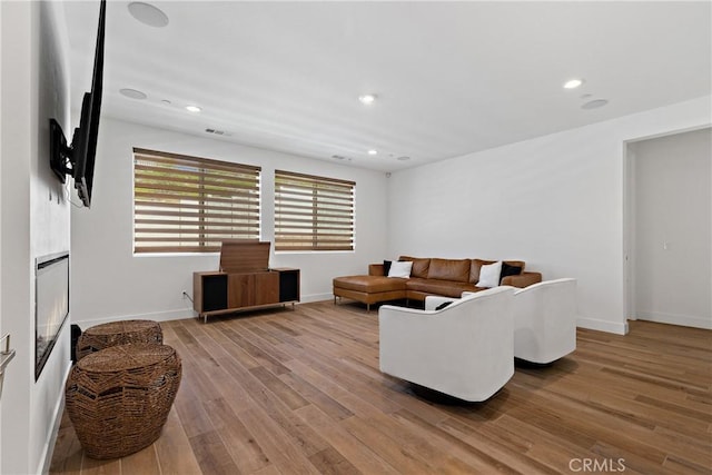 living area with light wood-style floors, baseboards, a glass covered fireplace, and recessed lighting
