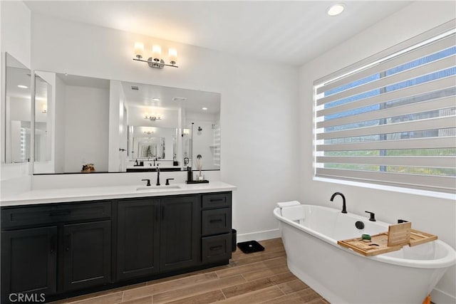 full bathroom with wood finished floors, vanity, a shower stall, a freestanding bath, and baseboards