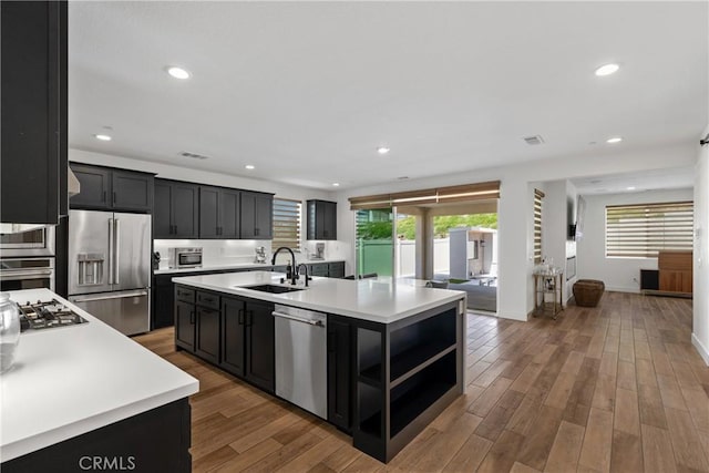 kitchen featuring stainless steel appliances, a sink, dark cabinetry, light countertops, and recessed lighting
