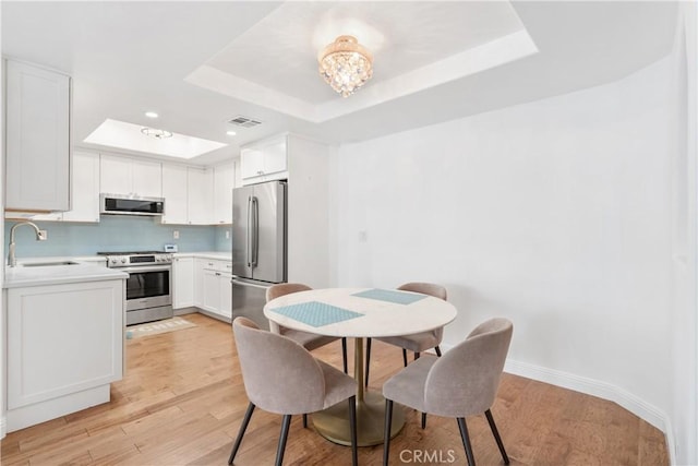 dining room with a raised ceiling, light wood-style flooring, baseboards, and recessed lighting