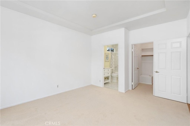 unfurnished bedroom with light carpet, a walk in closet, a closet, ensuite bath, and baseboards