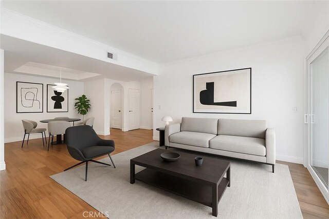 4230 Colfax Ave Unit 103, Studio City, CA 91604 - living room with arched walkways, light wood-style floors, baseboards, ornamental molding, and a tray ceiling