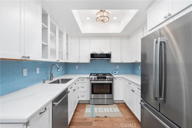 kitchen featuring stainless steel appliances, a sink, a raised ceiling, backsplash, and light wood-style flooring