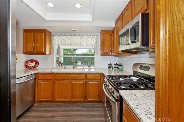 kitchen with appliances with stainless steel finishes, a sink, a tray ceiling, brown cabinetry, and ornamental molding
