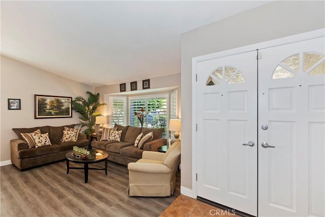 living area with baseboards, vaulted ceiling, and light wood-type flooring