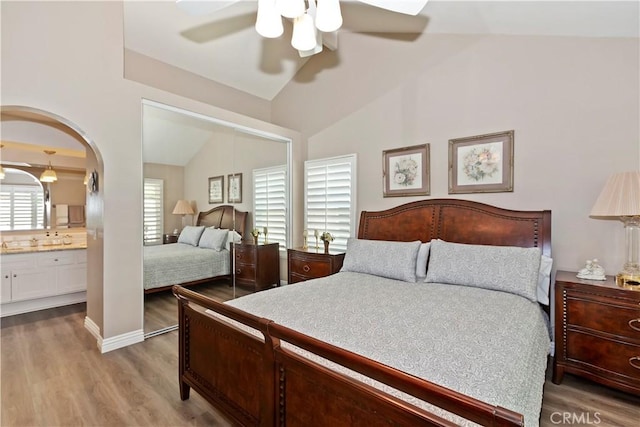 bedroom featuring wood finished floors, lofted ceiling, ceiling fan, ensuite bathroom, and arched walkways