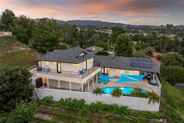 5150 Mountain Springs Ranch Rd, La Verne, CA 91750 - back of property at dusk featuring solar panels, a fenced backyard, a patio, an outdoor pool, and stucco siding