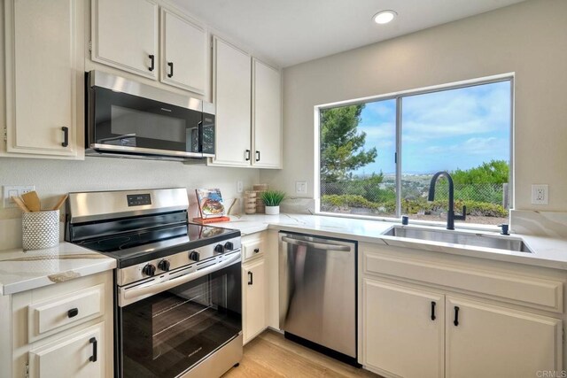 kitchen with appliances with stainless steel finishes, a sink, light countertops, and recessed lighting