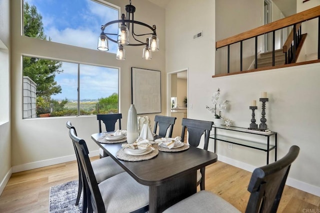 dining space with a chandelier, baseboards, light wood-type flooring, and a high ceiling