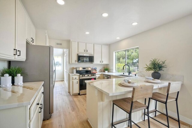 kitchen featuring stainless steel appliances, a sink, a peninsula, light wood-style floors, and recessed lighting