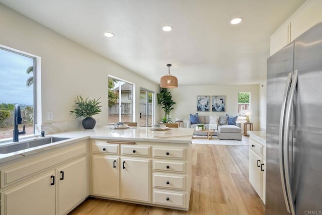 kitchen with freestanding refrigerator, a sink, light countertops, a peninsula, and light wood-type flooring