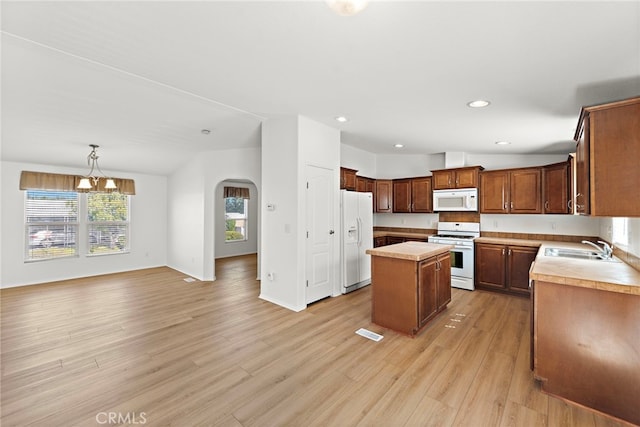kitchen with white appliances, a sink, a center island, light countertops, and arched walkways