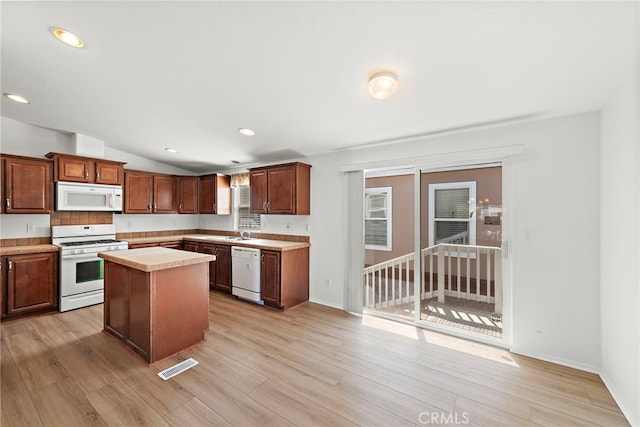 kitchen with white appliances, light countertops, a sink, a center island, and light wood finished floors