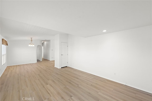 unfurnished room with light wood-style floors, recessed lighting, arched walkways, a chandelier, and baseboards