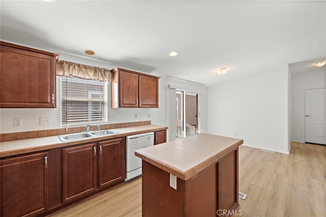 kitchen featuring white dishwasher, a sink, light wood-style floors, a kitchen island, and light countertops