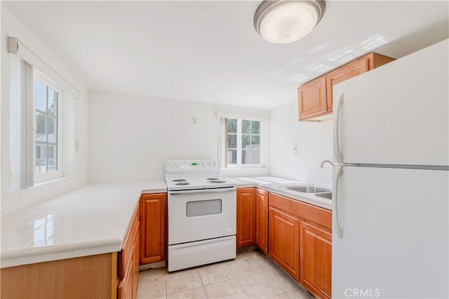kitchen featuring white appliances, a sink, light countertops, light tile patterned flooring, and brown cabinetry